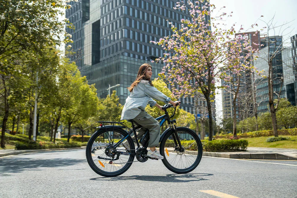 DUOTTS electric commuter bike being ridden by woman on sunlit city street with modern skyscraper backdrop