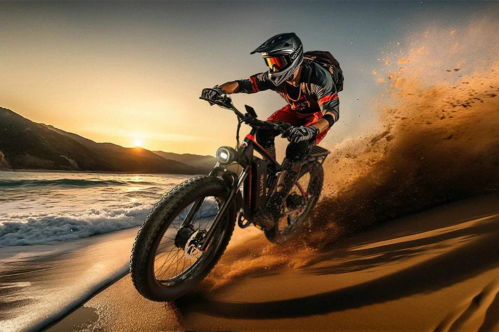 Lifestyle shot of a rider in full gear riding a black fat-tire electric bike with red accents on a sandy beach at sunset, kicking up sand spray with ocean waves and mountains in the background