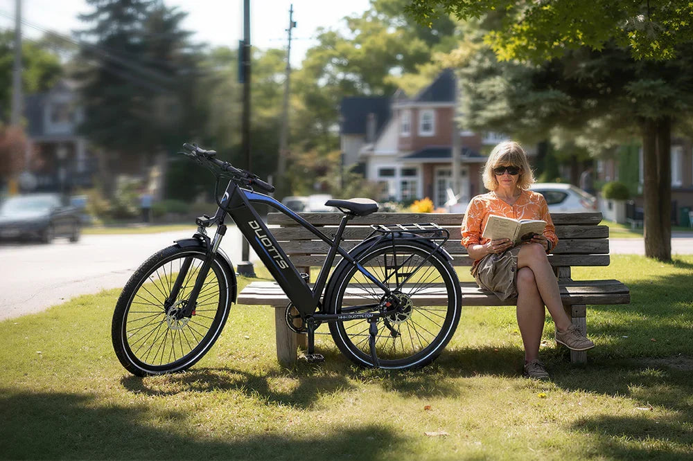 Black DUOTTS electric bike with rear rack resting by park bench in suburban setting